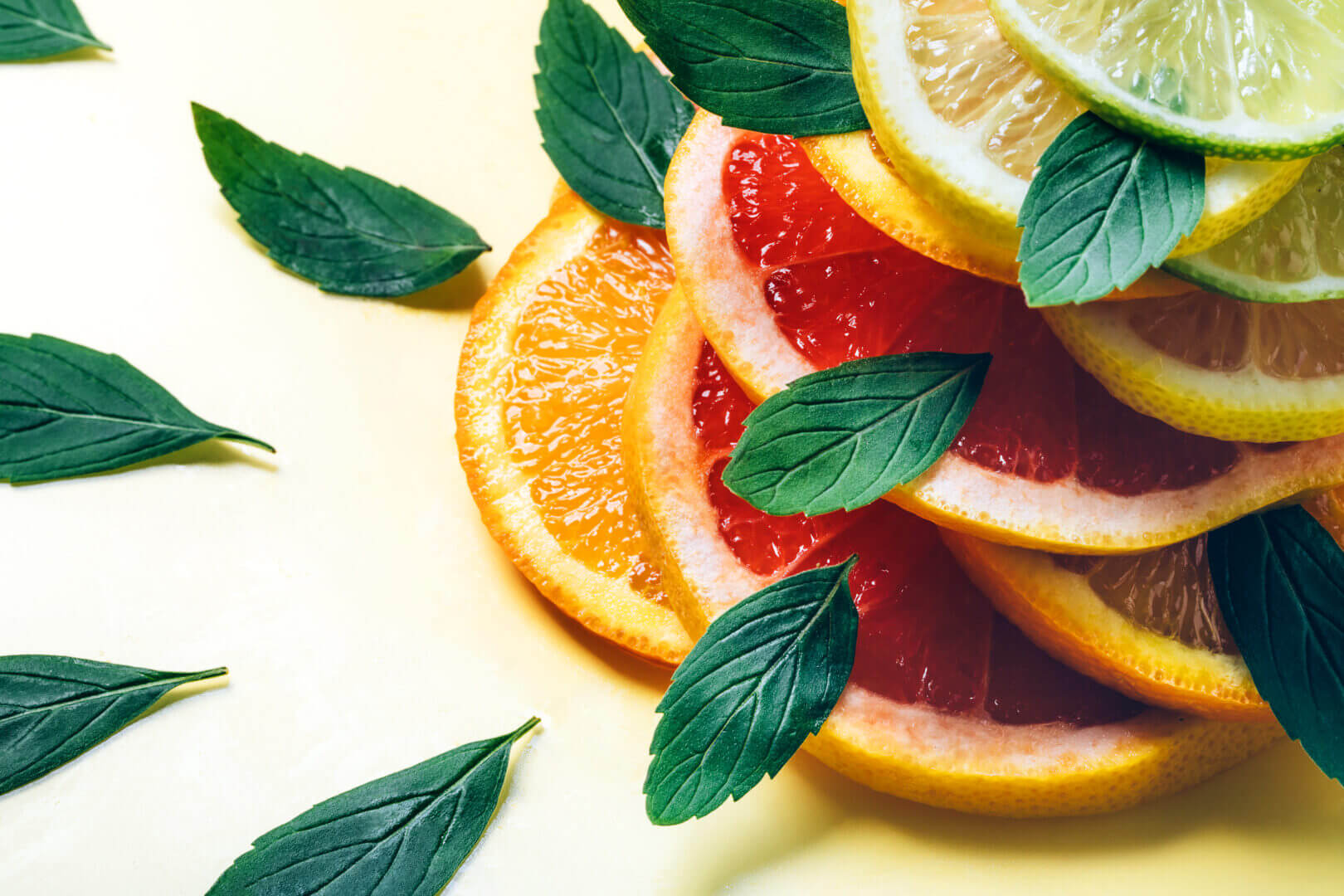 Citrus lemon, lime, orange and grapefruit slices and mint leaves in pile on yellow background.