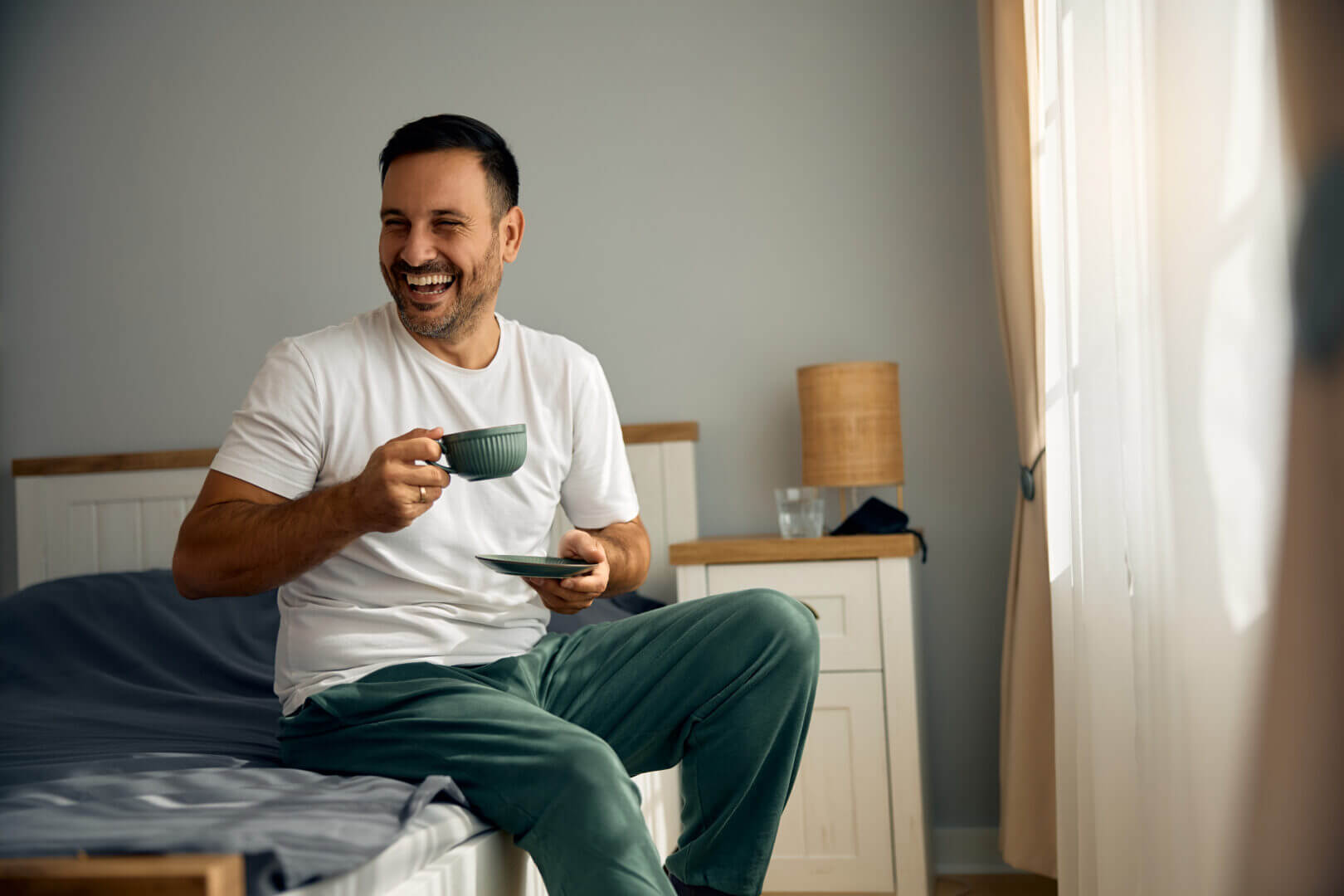 Happy man having cup of coffee in bedroom in the morning.