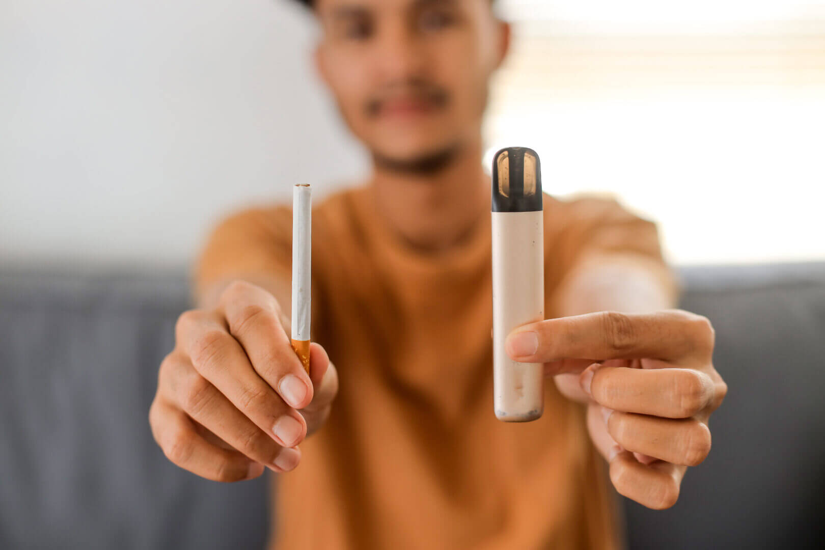 Young bearded man offers a choice between tobacco cigarette or electronic cigarette